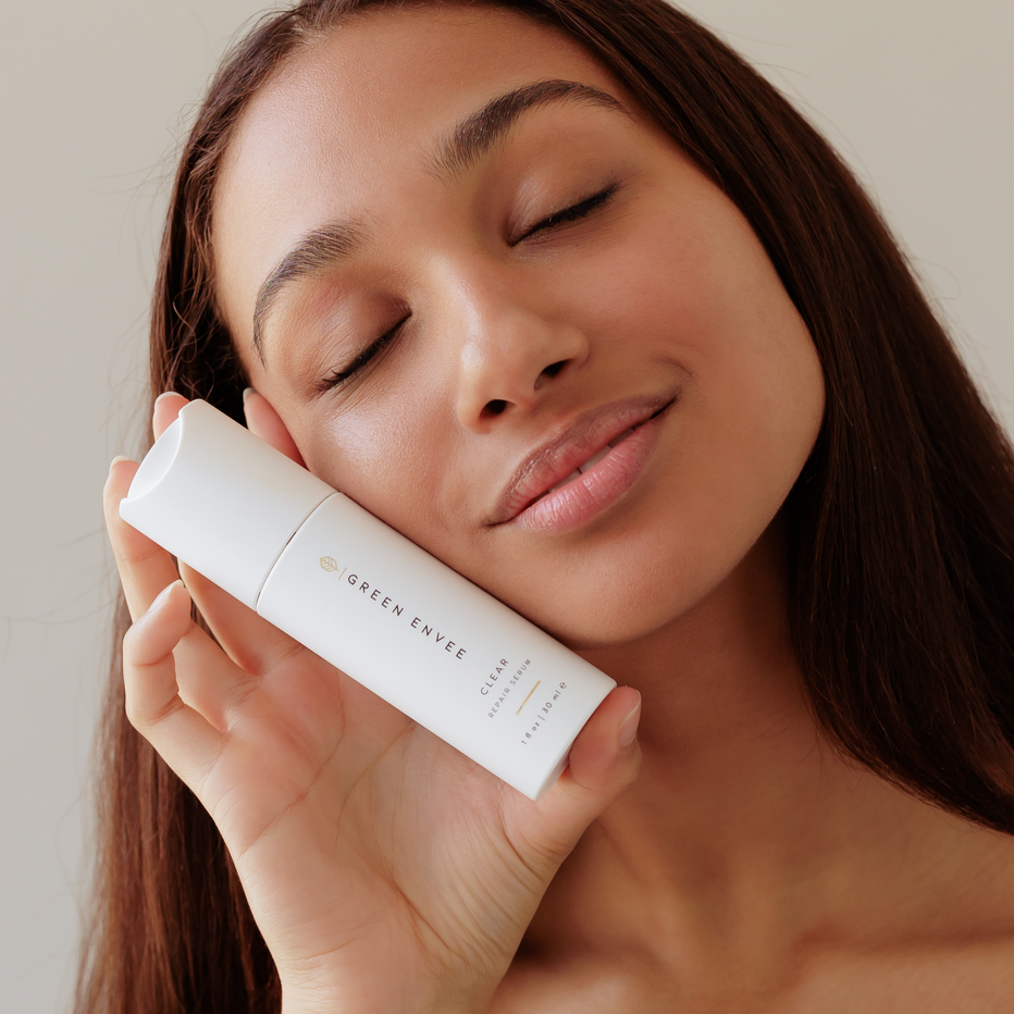 Woman holding a skincare product with 'Green Envee' branding against a neutral background. Label showing Clear Repair Serum