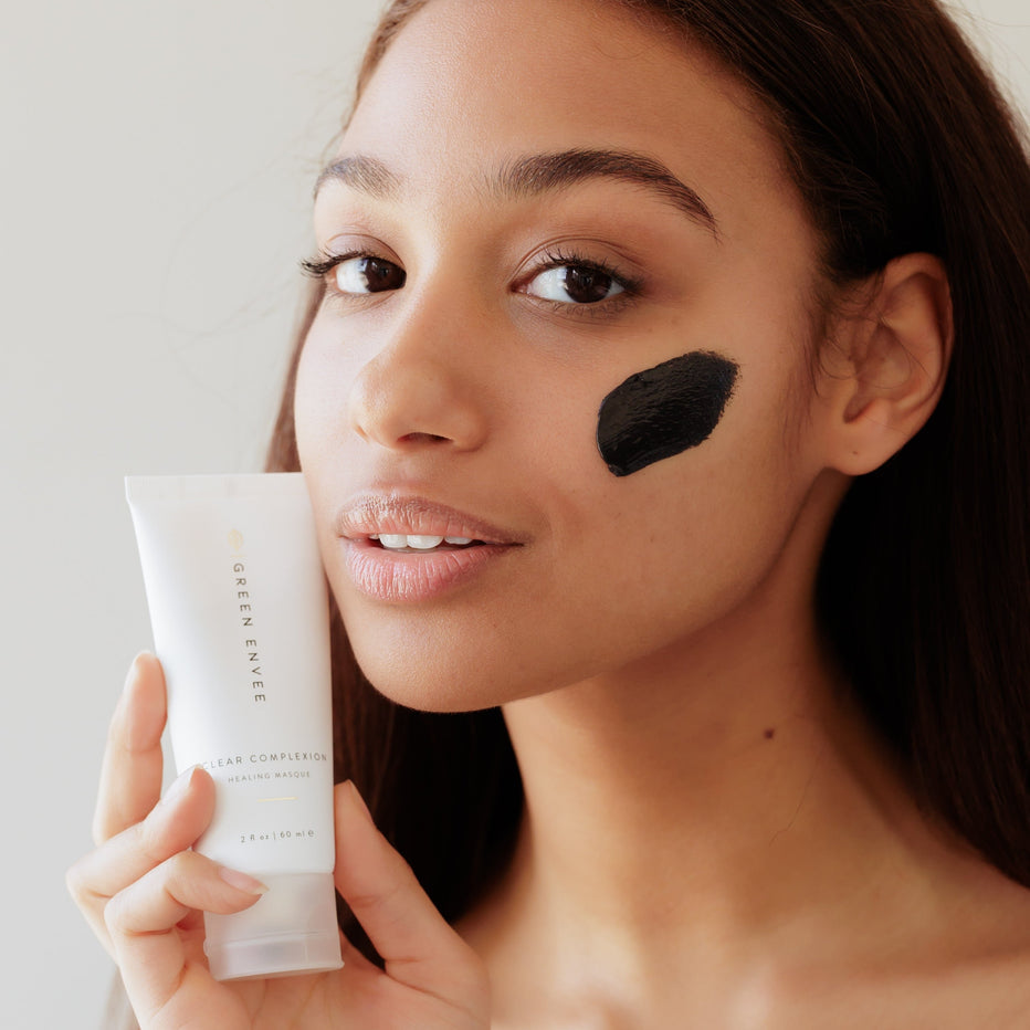 Woman holding a green envee skincare product tube of charcoal healing Masque with a neutral background