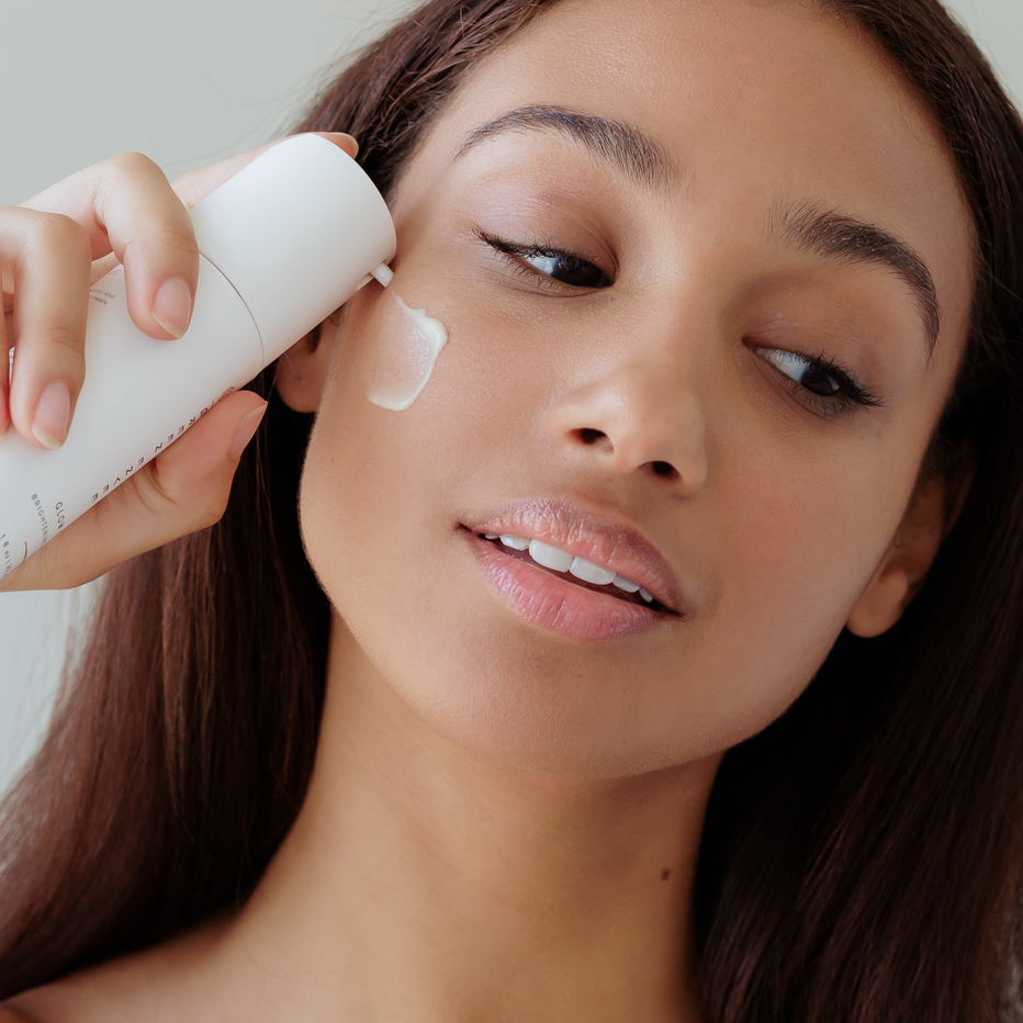 Woman applying Green Envee Glow Serum to her face with a focus on skincare routine.
