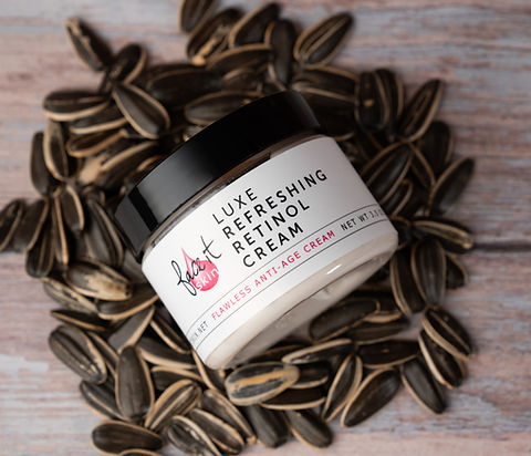 Jar of Luxe Refreshing Retinol Cream surrounded by sunflower seeds on a wooden surface
