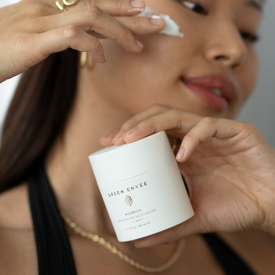 Woman applying cream to her face with a container of 'Green Envee' product.