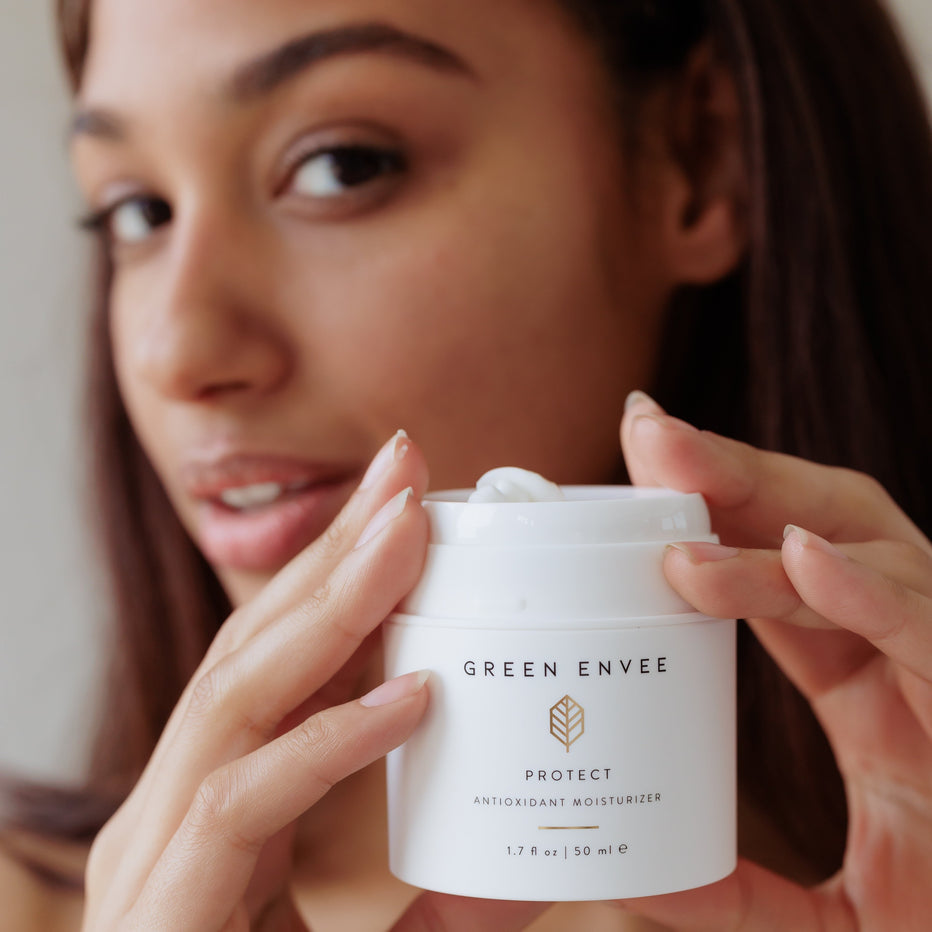 Woman holding a jar of Green Envee skincare product, labeled Protect Antioxidant