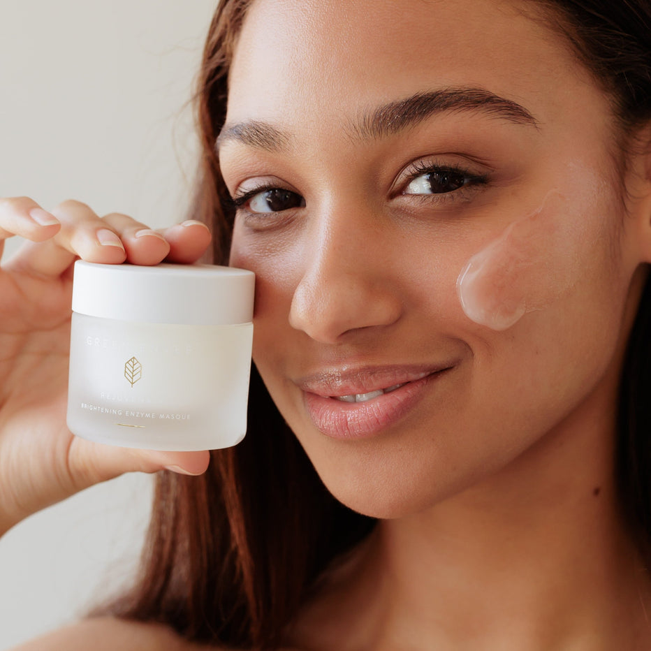 Woman applying cream to her face with a jar of Green Envee Masque. Facial mask