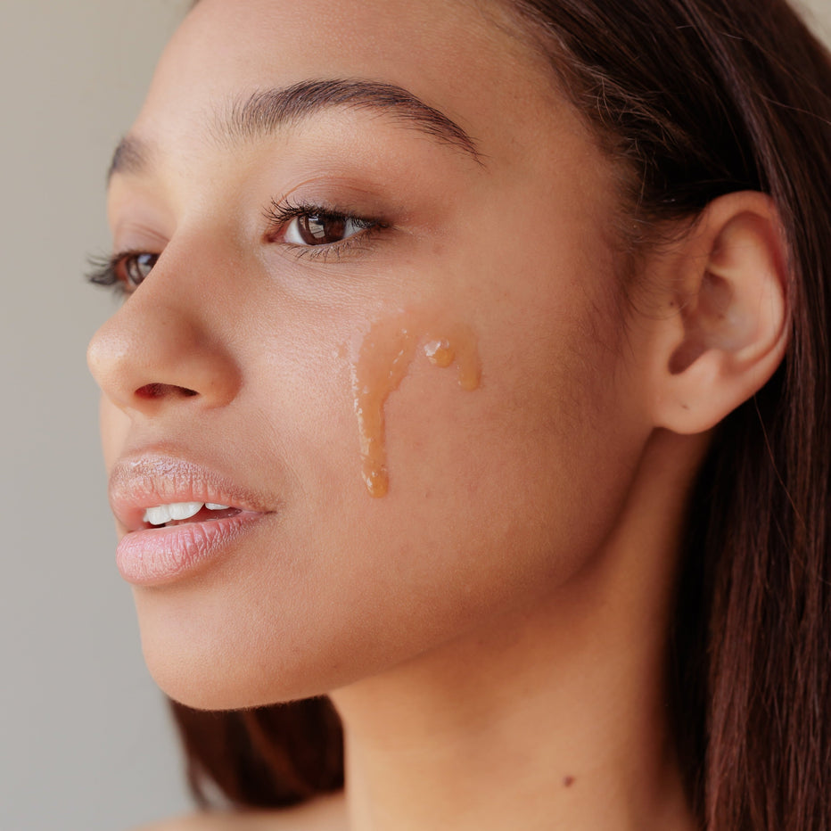 Close-up of a woman's face with a Green Envee retinal anti-aging cosmetic product applied to her cheek.