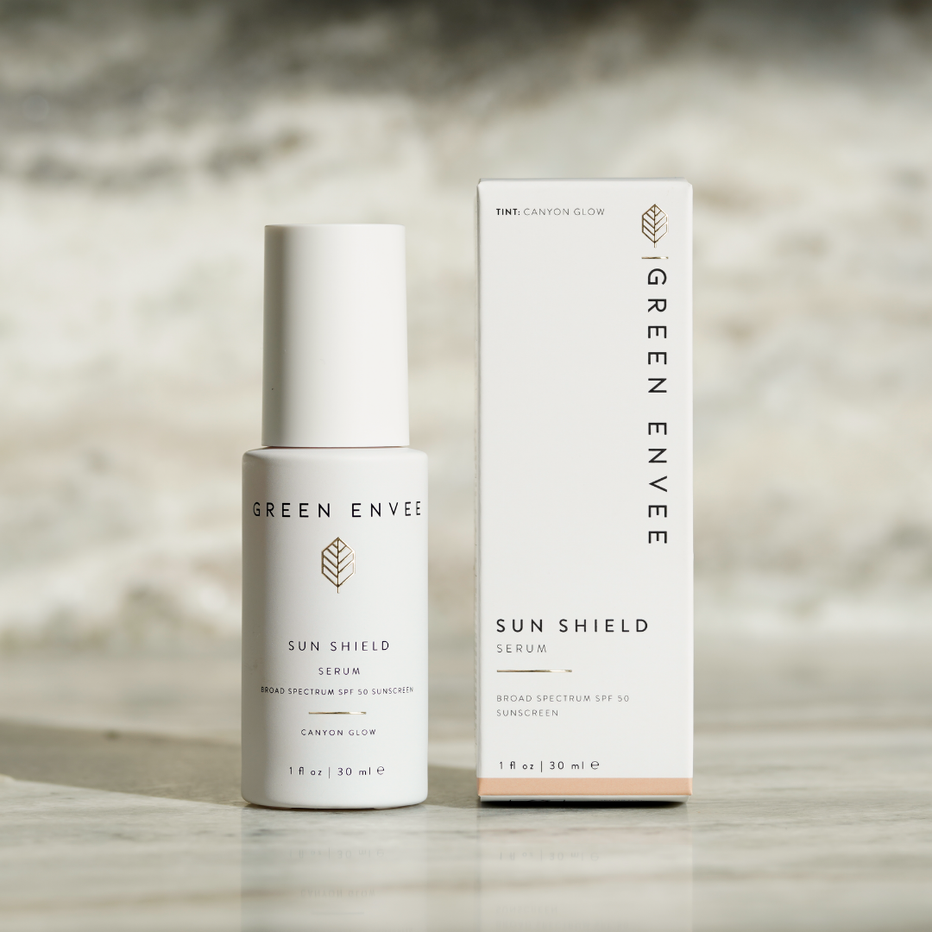 Green Envee Sun Shield Serum (sun screen spf 50) bottle and packaging on a wooden surface with a blurred background
